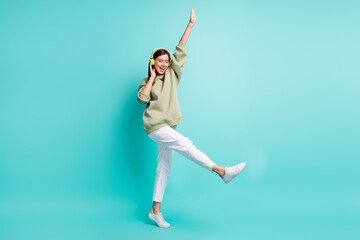 Full length photo portrait of cool woman wearing green headphones dancing standing on one leg isolated on vivid turquoise colored background