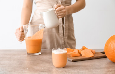 Woman preparing tasty pumpkin smoothie at table