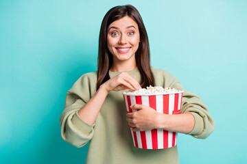 Photo portrait of immersed excited woman holding large popcorn bucket eating isolated on vivid turquoise colored background