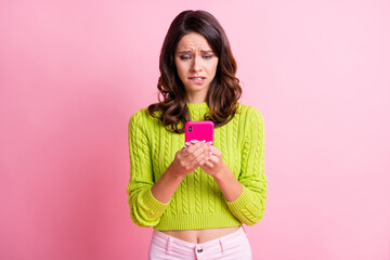 Photo of nervous young girl hold smartphone bite lip wear green sweater isolated pink color background