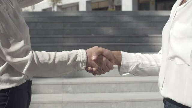 Unrecognizable businesswomen standing outside and handshaking. Confident successful partners in white blouses concluding contract. Static camera. Closeup view. Business and partnership concept