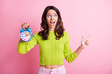 Photo of impressed wavy lady wear green sweater pointing finger empty space holding alarm isolated pink color background