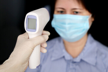 Coronavirus symptoms, doctor measures body temperature of woman in medical mask. Digital infrared...