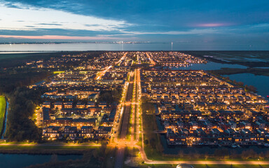 Modern residential neighbourhood in the city of Almere, The Netherlands, Amsterdam suburb, surrounded by water and nature. Aerial shot at dusk.