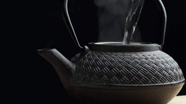 Brewing tea in cast iron tea pot, 2 shots - pouring hot water and putting a lid on