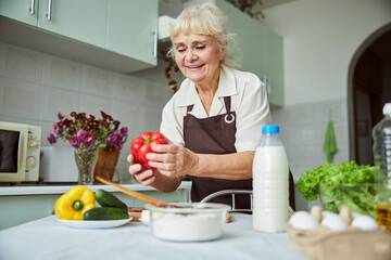 Joyful old woman cooking dinner at home