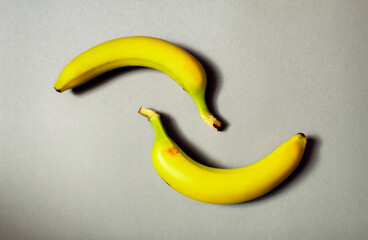Two yellow bananas placed on a grey background, creating a minimalist wavy shape. 