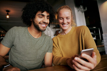 Portrait of happy couple using smartphone and smiling while sitting and relaxing in cafe