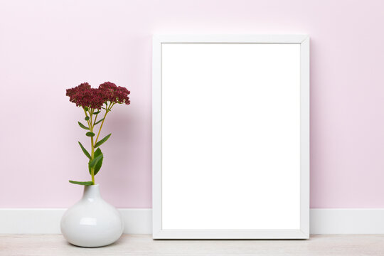 White vertical picture frame leaning on pink wall mockup  for online shop with sedum flowers in vase