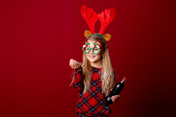 a little girl in Christmas glasses holding a bottle with a drink. Christmas concept, red background, text space