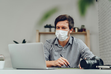 Man working on laptop at home and wearing medical mask