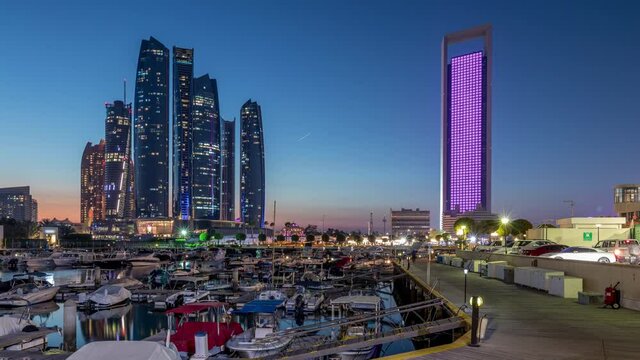 Al Bateen marina Abu Dhabi day to night timelapse after sunset with boats in harbor and illuminated modern skyscrapers on background