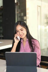 Portrait of a young businesswoman is talking on mobile phone while working with computer tablet in office.