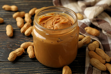 Peanut, napkin and jar with peanut butter on wooden background
