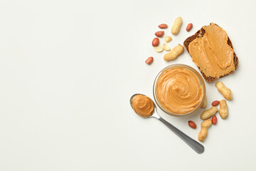 Jar, spoon and sandwich with peanut butter on white background