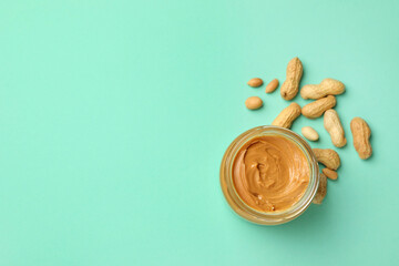 Jar with peanut butter and peanut on mint background