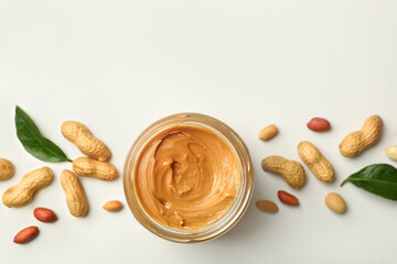Jar with peanut butter, peanut and leaves on white background