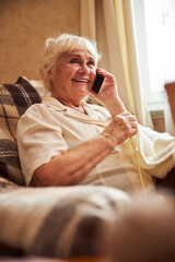Joyful senior woman talking on mobile phone and home