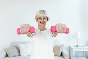 Fototapeta na wymiar Senior woman exercise with dumbbells at home . happy mature woman doing arm workout using dumbbells. Elderly woman prefers healthy lifestyle