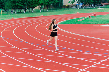 A female coach with dark hair stands on the red running track of the stadium