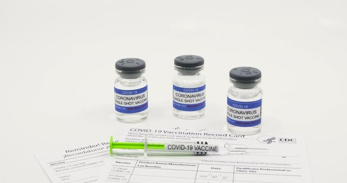 Doctor with blue gloves placing syringe with COVID-19 vaccine on vaccination record card approved by CDC with corona virus vaccine vials in the background. Concept on white background with copy space.