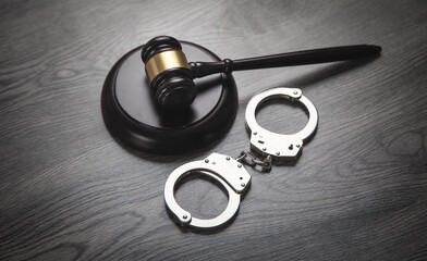 Metal handcuffs and judge gavel on the dark background.