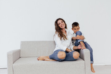 Fototapeta na wymiar Mom and young son sit at home on a white sofa