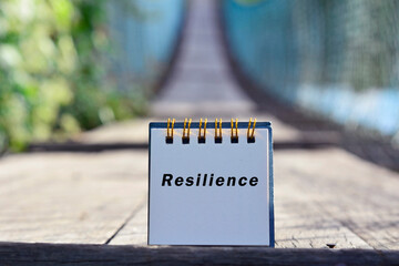 Resilience text written on white note with blurred background of hanging bridge