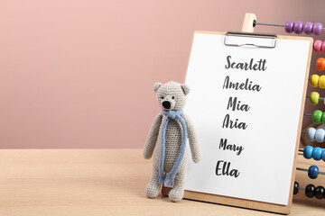 Clipboard with list of baby names and toys on wooden table. Space for text