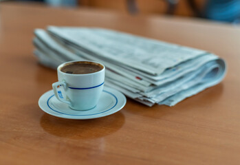 A cup of Turkish coffee and newspaper on the wooden table.