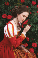 beautiful young woman in a red medieval style dress is sitting in the garden and smelling roses, fantasy princess © Анастасія Смирнова