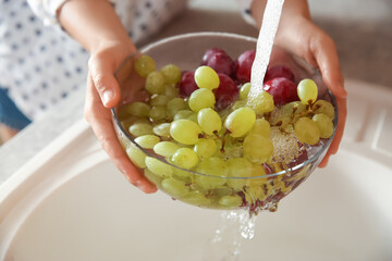 Woman washing fresh grapes in kitchen sink, closeup - Powered by Adobe