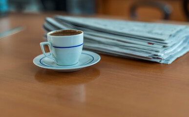 A cup of Turkish coffee and newspaper on the wooden table.