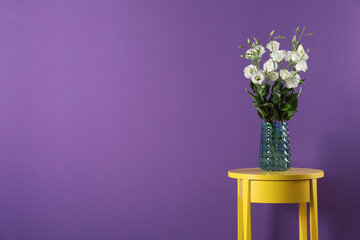 Elegant vase with eustoma flowers on table near purple wall. Space for text