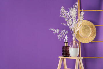 Stylish vases with beautiful branches near purple wall. Space for text