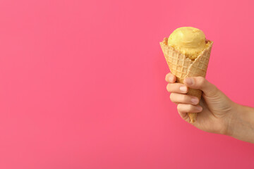 Woman holding waffle cone with delicious yellow ice cream on pink background, closeup. Space for...