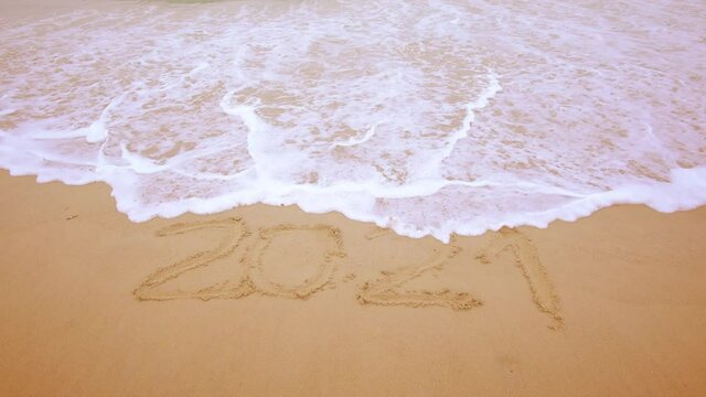 2020-2021 Change New year on the beach. 2020 handwritten sand texture  The water wave erased and changed to 2021. 