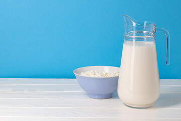 Glass pitcher of milk and bowl of cottage cheese on wooden table