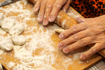 a woman makes dumplings with her hands on a wooden cutting Board rolls out the dough with a wooden rolling pin