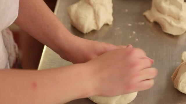 Baker's Hands Kneading Bread Dough On Stainless Tabletop In The Kitchen - close up
