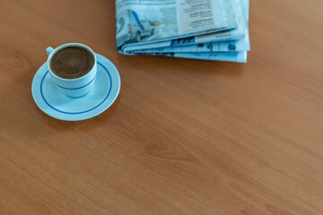 A cup of Turkish coffee and newspaper on the wooden table.