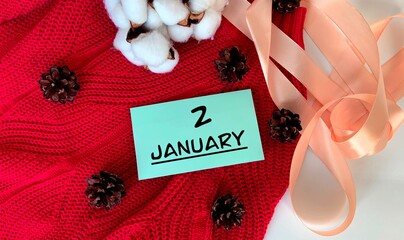 January 2 on a piece of paper.Cones, cotton, ribbon and a knitted sweater on a white background .Winter.Calendar for January.