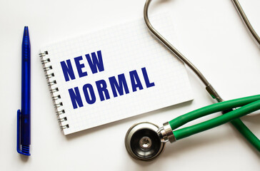 NEW NORMAL is written in a notebook on a white table next to pen and a stethoscope.