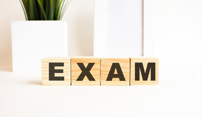 Wooden cubes with letters on a white table. The word is EXAM. White background.