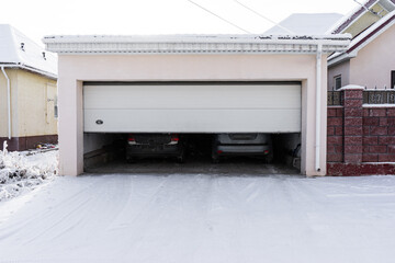 xterior of a  garage attached to a house. garage with two cars inside in winter. semi-open...