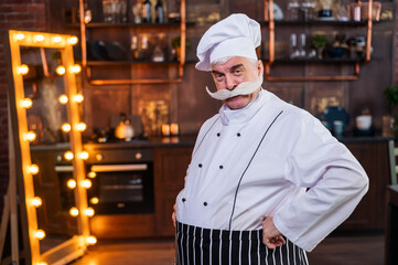 Serious elderly male chef posing in the kitchen