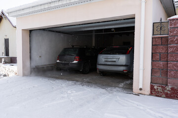 xterior of a  garage attached to a house. garage with two cars inside in winter. semi-open sectional  doors
