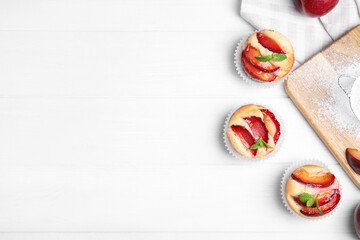 Delicious cupcakes with plums on white wooden table, flat lay. Space for text