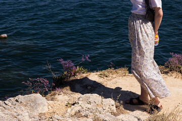 Female wearing skirt and sandals standing near blue sea. Copy space next to girl. Summer sunlight, nature