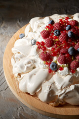 food, culinary, baking and cooking concept - close up of pavlova meringue cake decorated with berries on wooden serving board